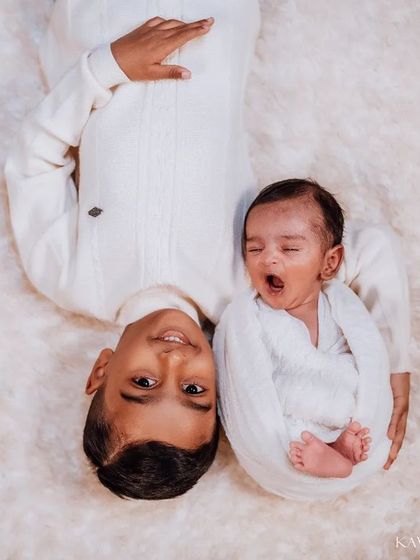 A creative overhead shot showing the two brothers side-by-side. The sleepy newborn's yawn next to his smiling big brother captures a real, unposed moment.