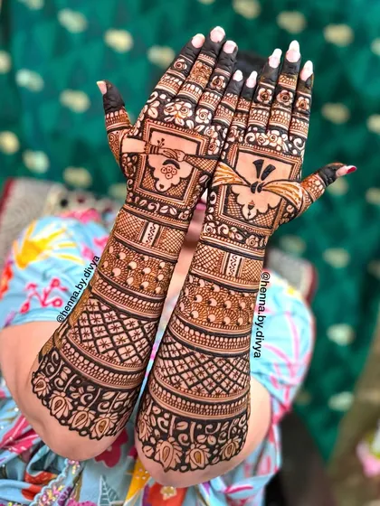 A beautiful shot of a bride showcasing her full-coverage mehendi. The design features traditional 'dulha-dulhan' (bride and groom) figures and intricate grid work.