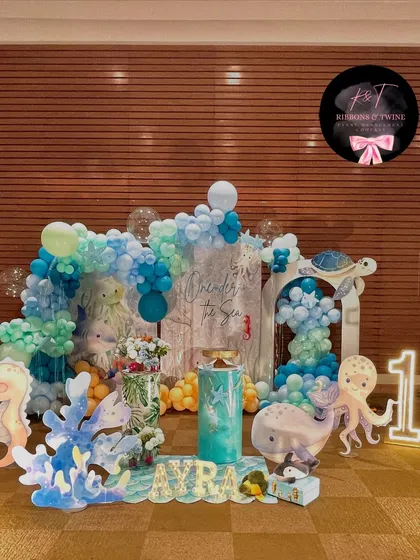 An enchanting 'One-der the Sea' first birthday celebration for baby Ayra. This full view showcases the cohesive underwater theme with blue balloon waves, adorable sea creature cutouts, and personalized marquee letters.