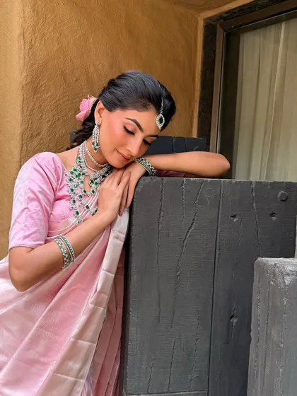 A serene and contemplative moment. The soft lighting highlights the dewy finish of her makeup and the shimmer of her pink Kanjeevaram saree.