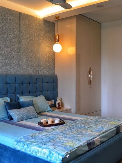 A master bedroom from our Casa Savera project, designed with a calming blue theme. The space features a large tufted blue headboard, a textured wallpaper accent wall, and warm pendant lights.