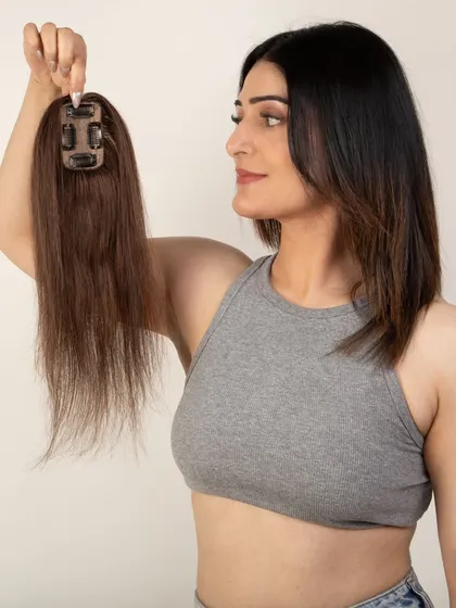 A model holding a hair topper by its clips, showing the underside and application mechanism.