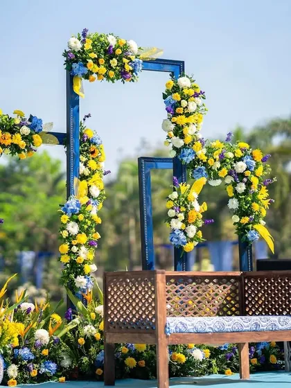 A modern and artistic Haldi seating area, using blue geometric frames adorned with yellow and blue flowers for a unique and colorful look.