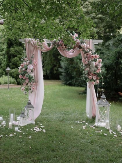 A romantic garden photo booth with a simple arch draped in blush pink fabric and flowers.