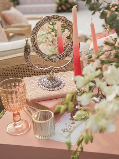 A close-up of a tabletop detail, featuring an ornate silver mirror, ombre candles, and custom stationery.
