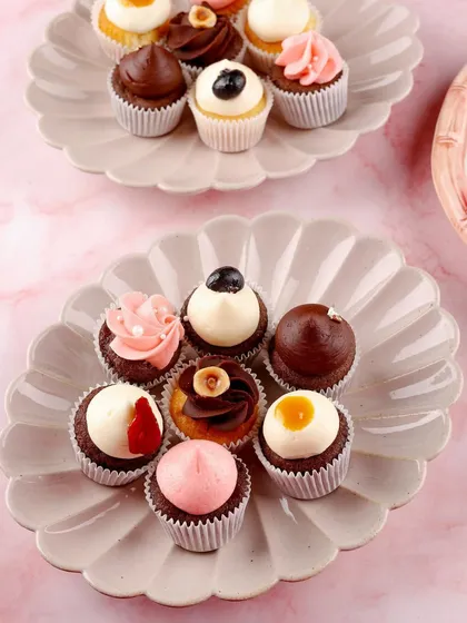 An assortment of mini cupcakes, showcasing a variety of frostings and toppings. Perfect for festive menus or catering services.