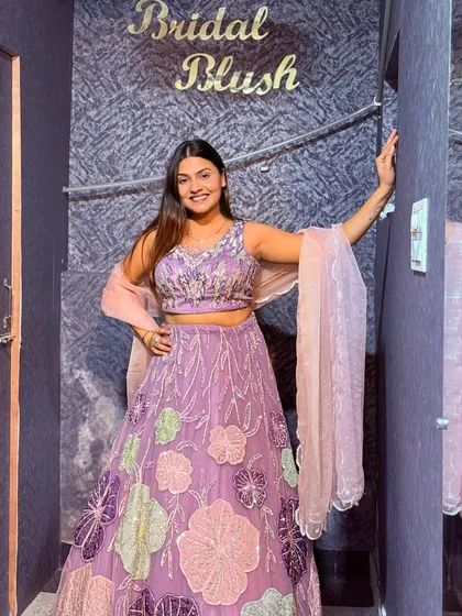A happy client posing in front of the Bridal Blush sign. She looks lovely in this lavender floral lehenga, perfect for a friend's wedding.