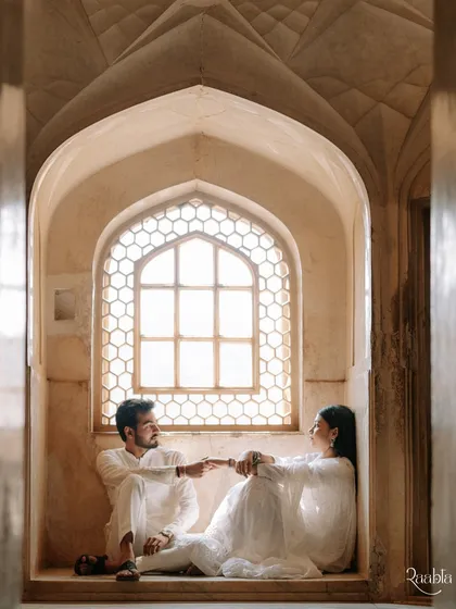 A romantic portrait of the couple seated in a Jharokha, a classic window seat in a Rajasthani palace, creating a timeless and intimate scene.
