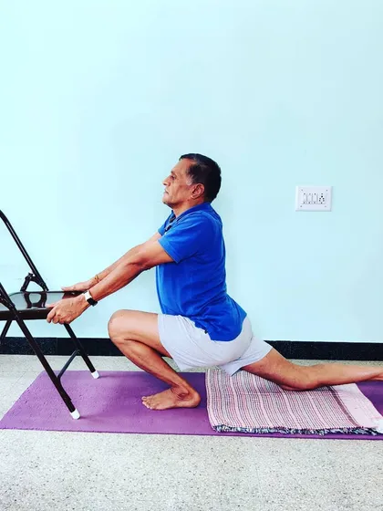 Eka Pada Prasaranaasana using a chair for support. This pose develops balance and hamstring flexibility. The chair helps stabilize the posture as you work on alignment.