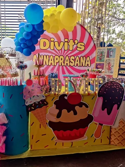 A colorful and sweet candy-themed Annaprasana ceremony. The decor is filled with giant ice cream cone and cupcake cutouts, a candy-striped backdrop, and bright balloon clusters.