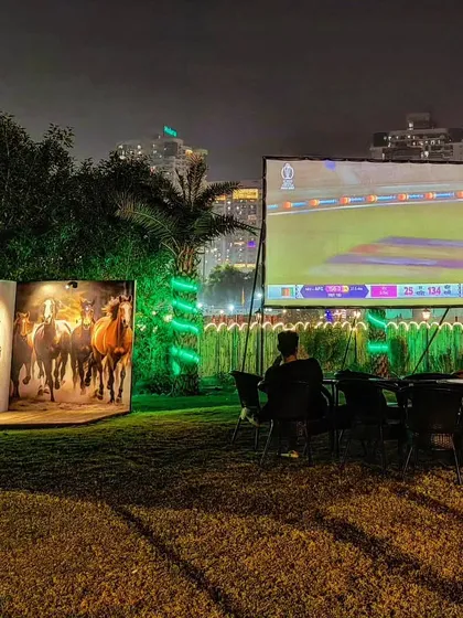 We host outdoor sports screenings on a giant projector, creating a mini-stadium feel. Here, guests enjoy a live cricket match on our lawn, a perfect setup for a community sports night.