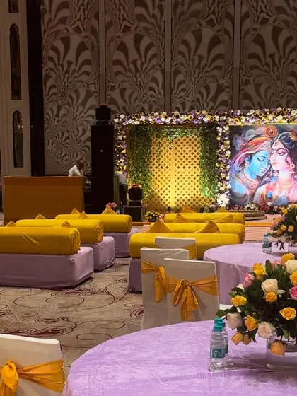 An overview of the seating arrangement for a Haldi function. The space combines traditional low floor seating with round tables, all decorated in a cohesive lilac and yellow color scheme.