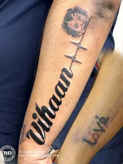 We turned a faded memory into a timeless tribute. This piece was designed to cover an old, colorful tattoo with the name of the client's son, "Vihaan," connected by a heartbeat line to his portrait. It's a beautiful example of how a cover-up can become the most meaningful tattoo of all.