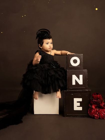 Posing like a little queen on her 'ONE' blocks. The long train of the black dress adds a touch of high-fashion drama to this first birthday photo.