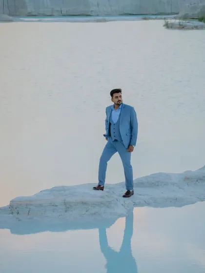 A powerful solo shot of the groom standing on the edge of the turquoise water. The reflection on the water's surface adds a beautiful, symmetrical element to the photograph.