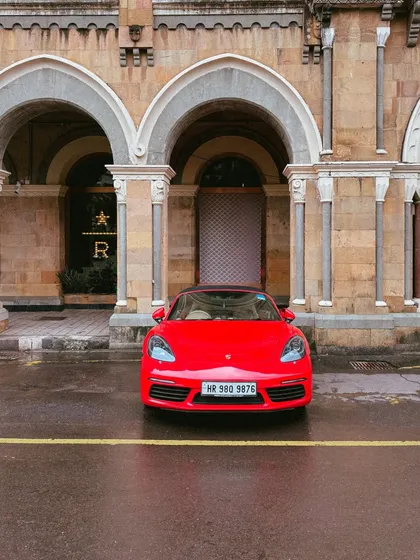 A head-on shot of the red Porsche, perfectly centered against the grand arches of the heritage building. The yellow line on the road acts as a great leading line.