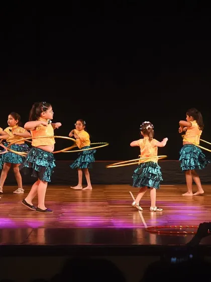 A wide view of the hoop dance performance, with the audience visible in the foreground. This shows the scale of our student showcases and the professional environment we provide.