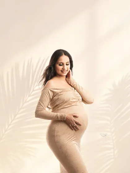 A lovely three-quarter shot of a mom-to-be in a fitted beige off-shoulder gown. The soft lighting and gentle pose create a warm and intimate portrait.