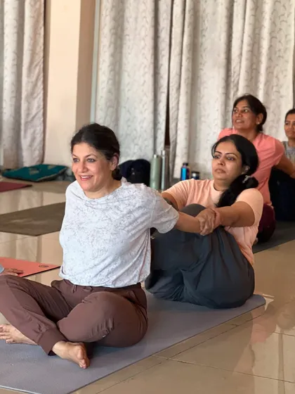 A student assists another in Ardha Matsyendrasana, fostering a supportive learning environment. The group energy motivates everyone to go deeper in their practice.