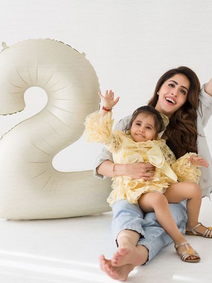A joyful, celebratory photo of a mother and her two-year-old daughter. Their waving hands and big smiles perfectly capture the fun of a birthday.
