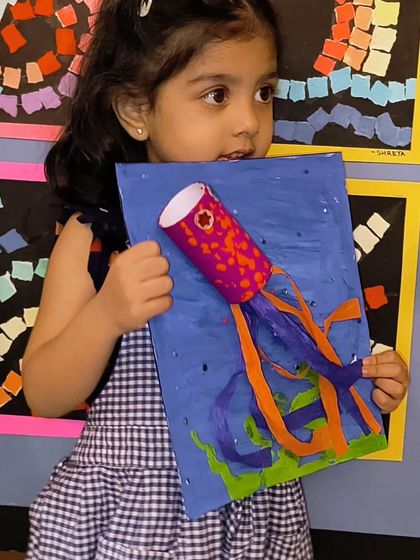 A young student proudly holds her 3D jellyfish craft. This project is great for learning about sea creatures while practicing cutting and construction skills.