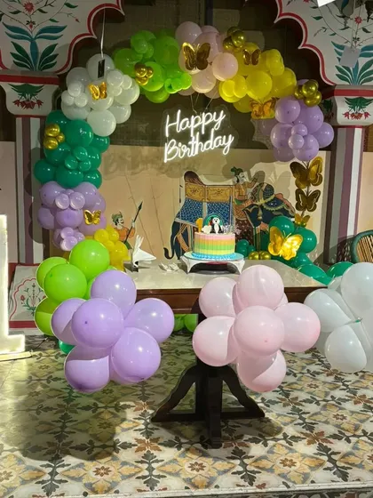 This colorful first birthday decoration was set up in a restaurant with a unique traditional backdrop. I integrated a rainbow balloon arch, a 'Happy Birthday' neon sign, and a marquee number '1' to create a festive party corner.