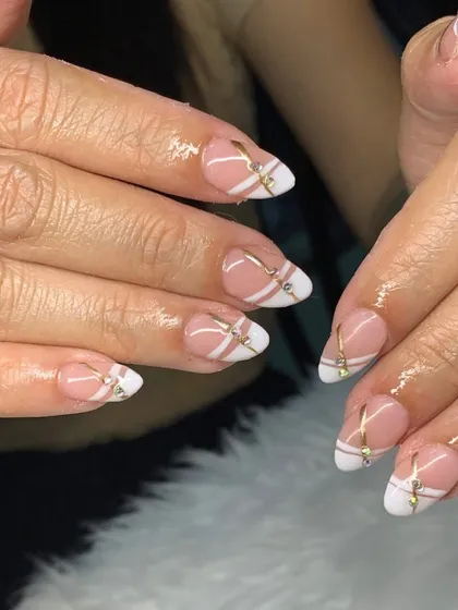 An elegant and modern design with a nude base, white tips, and delicate gold lines with rhinestone accents.