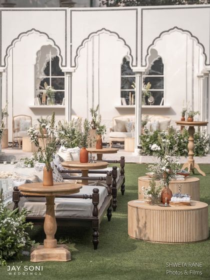 A mix of seating styles, including traditional Indian charpai-style daybeds and wooden tables, all unified by the elegant ivory and natural wood color scheme.
