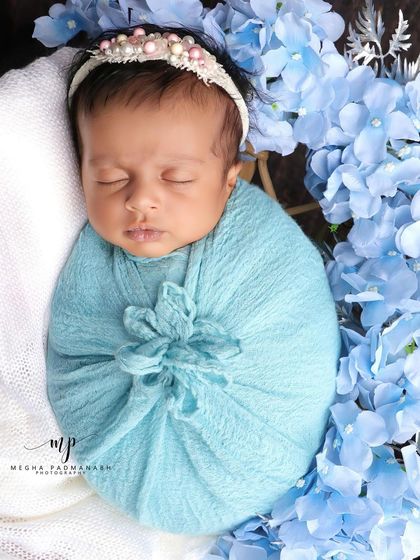 A close-up of a baby swaddled in blue, surrounded by a wreath of blue hydrangeas.