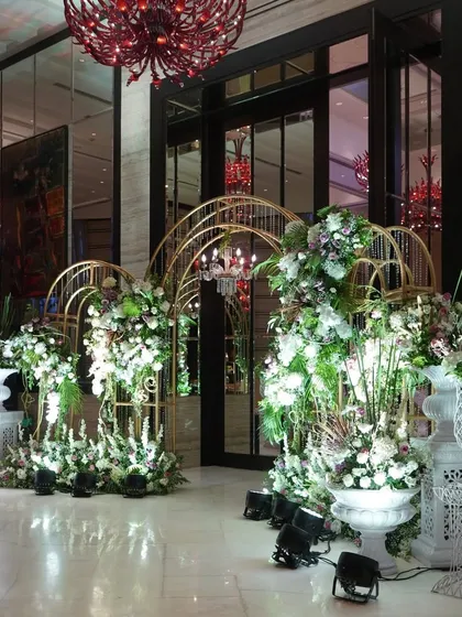 The entrance to this reception featured ornate golden arches overflowing with white flowers, creating a look of pure opulence and grandeur under the hall's dramatic red chandeliers.