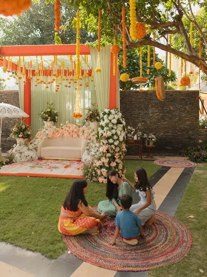 Creating relaxed spaces for guests is important. Here, guests sit on colorful jute rugs in the garden, enjoying the festive atmosphere of the daytime Mehendi.