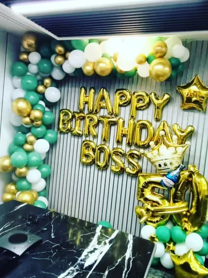 Another office party setup for a boss's 50th birthday. The decor features green, gold, and white balloons with a large foil crown.