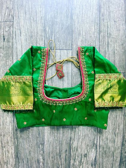 A green blouse with a contrasting pink border. The design uses the saree's gold Zari border on the sleeves.