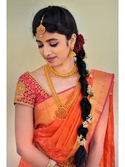 A soft, pretty look in an orange and pink saree. The makeup features pink tones on the eyes and lips, and the hair is styled in a traditional braid with flowers.