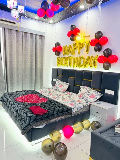 A close-up of a birthday bed decoration with 'Happy Birthday' foil balloons and a heart made from a red blanket.
