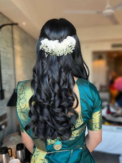 A classic half-up style with big, bouncy curls, adorned with a simple gajra of white flowers. This is a timeless look for any traditional event.