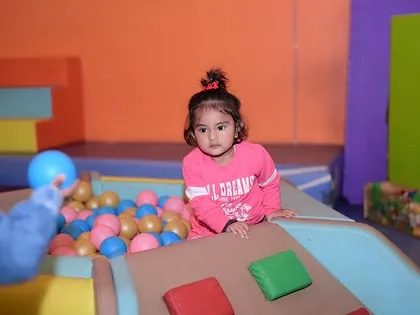 Peeking over the edge of the ball pit. Our play structures are designed to be engaging and encourage curiosity in a secure environment.