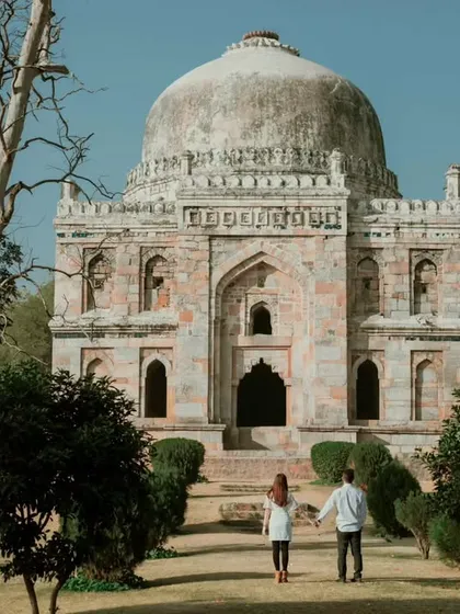 A stunning wide shot of a couple walking towards a magnificent tomb at Lodhi Garden, Delhi. This image captures the sense of grandeur and history that makes for an epic destination pre-wedding shoot.