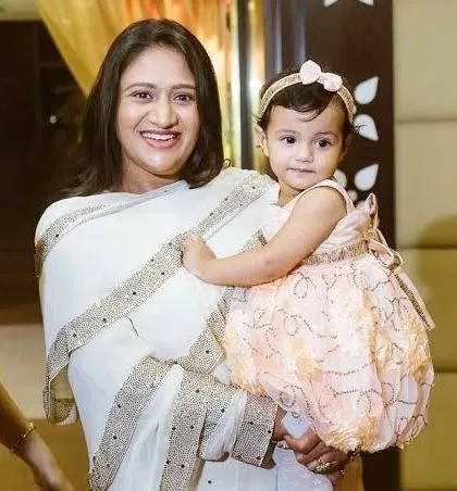 A mother in an elegant white saree smiles brightly while holding her young daughter. This is a beautiful portrait of motherly love and joy.