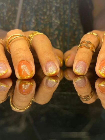 A warm and shimmery manicure with a mix of orange and glittery nude polishes.
