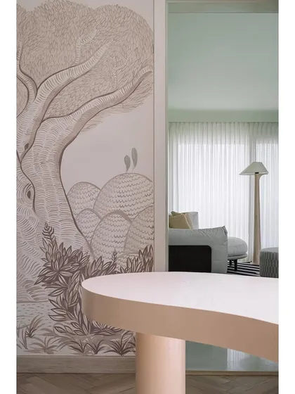 Another perspective of the den, where a peach-toned table sits in front of the whimsical, hand-painted wall mural. The design is all about creating enjoyable and visually interesting spaces.