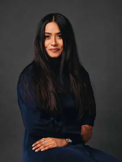 A classic seated headshot. The lighting is soft and flattering, and the expression is confident and engaging.