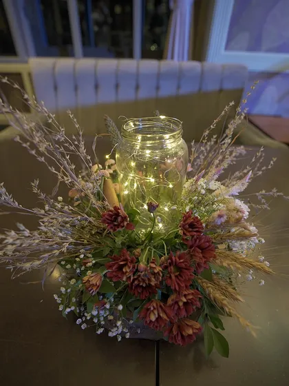 A rustic centerpiece with dried flowers and fairy lights in a glass jar. This enchanting design is perfect for creating a warm and cozy atmosphere at an evening event.