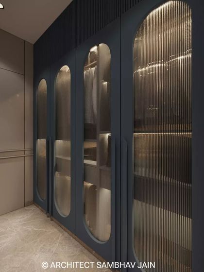 Elevate your storage experience with this opulent walk-in wardrobe, showcasing fluted glass panels framed in rich navy hues and complemented by soft, ambient lighting. The sleek marble flooring and bespoke design exude sophistication.