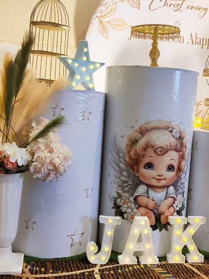 A close-up of the Christening decor for baby Jake, showing the angel-themed plinth and 'JAKE' marquee letters.