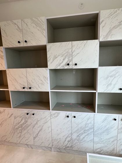 This custom storage unit features a marble-laminate finish and minimalist black knobs. The asymmetrical design provides a mix of open and closed shelving for both display and concealed storage.