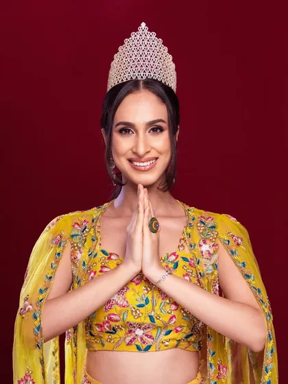 A portrait capturing the humility and grace of a winner. The 'namaste' pose and the crown create a powerful and inspiring image.