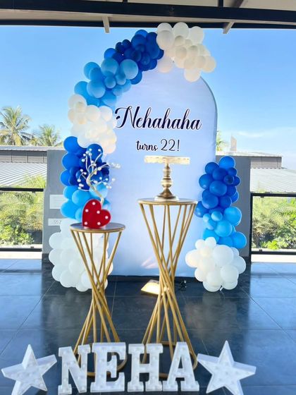 A bright and airy outdoor birthday setup for a 22nd birthday. The simple design features a white arched backdrop, a blue and white balloon garland, and elegant gold dessert stands.