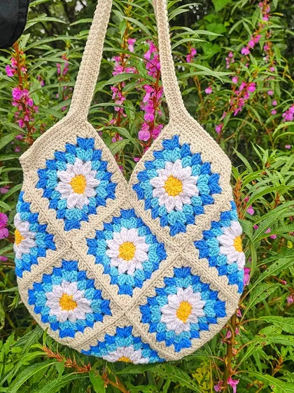 The Daisy Tote bag looking beautiful against a natural, floral background. The colors of the bag pop, showing how a handmade accessory can brighten up any look.