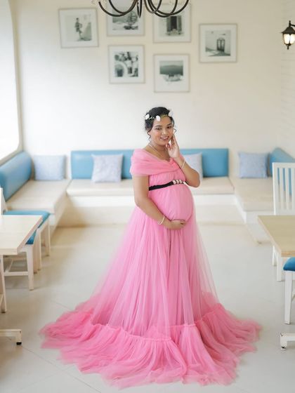 A solo portrait showcasing our popular off-shoulder pink maternity gown. The ruffled train and simple black belt create a chic and elegant look.